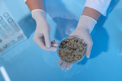 Photo of Laboratory testing. Scientist holding petri dish with sand sample at table, above view