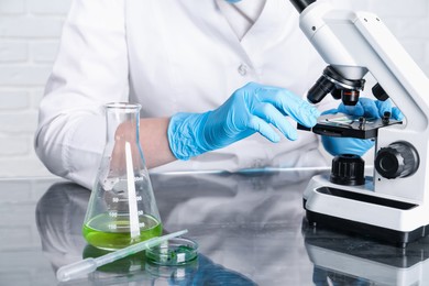 Photo of Laboratory testing. Scientist examining sample under microscope at table indoors, closeup