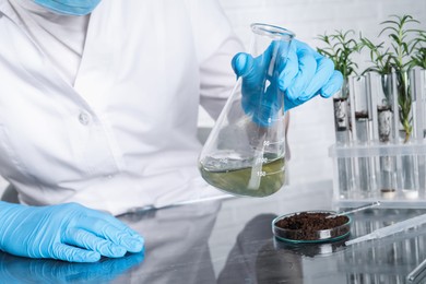 Photo of Laboratory testing. Scientist holding flask with sample at table indoors, closeup