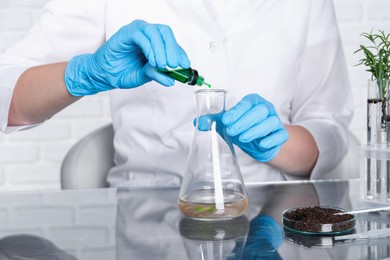 Photo of Laboratory testing. Scientist dripping liquid into flask with sample at table indoors, closeup