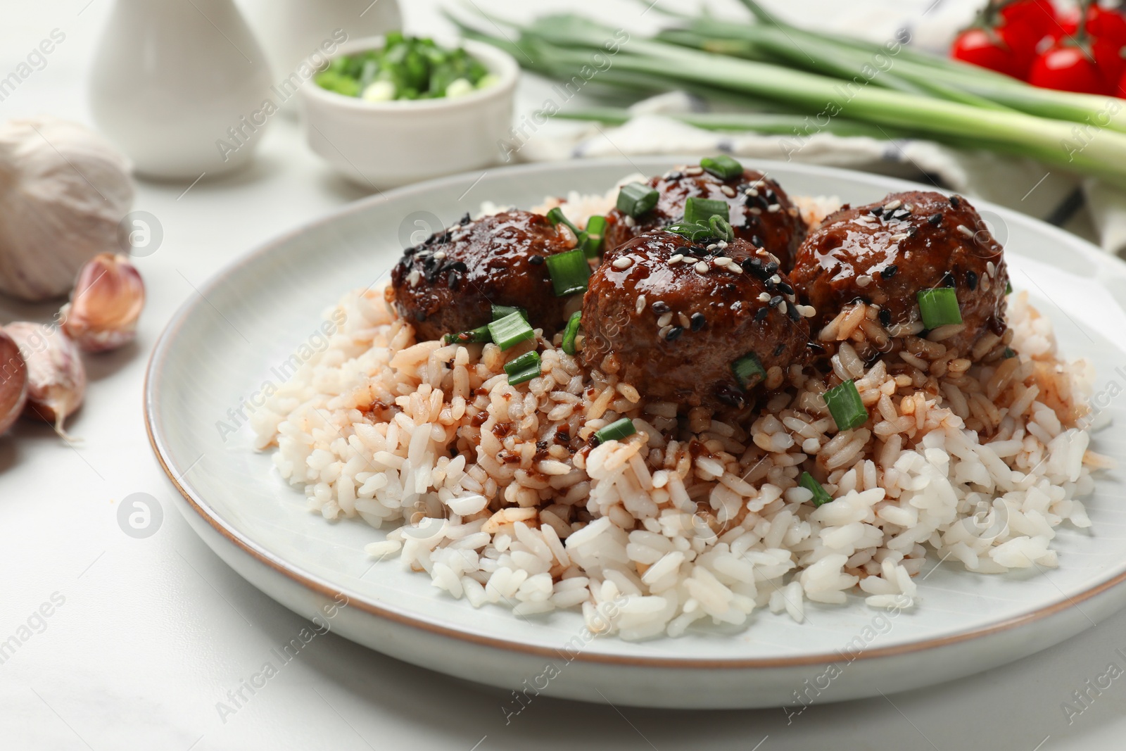 Photo of Delicious rice with meatballs, sauce and green onions on white table, closeup