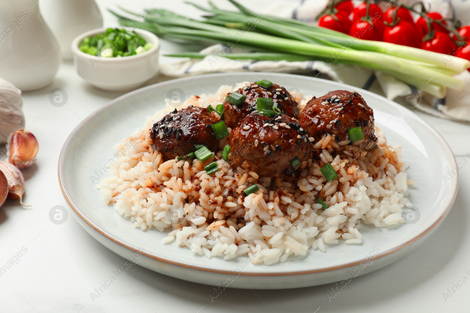 Photo of Delicious rice with meatballs, sauce and green onions on white table, closeup