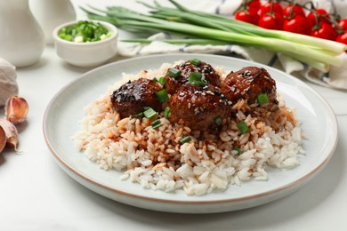 Photo of Delicious rice with meatballs, sauce and green onions on white table, closeup