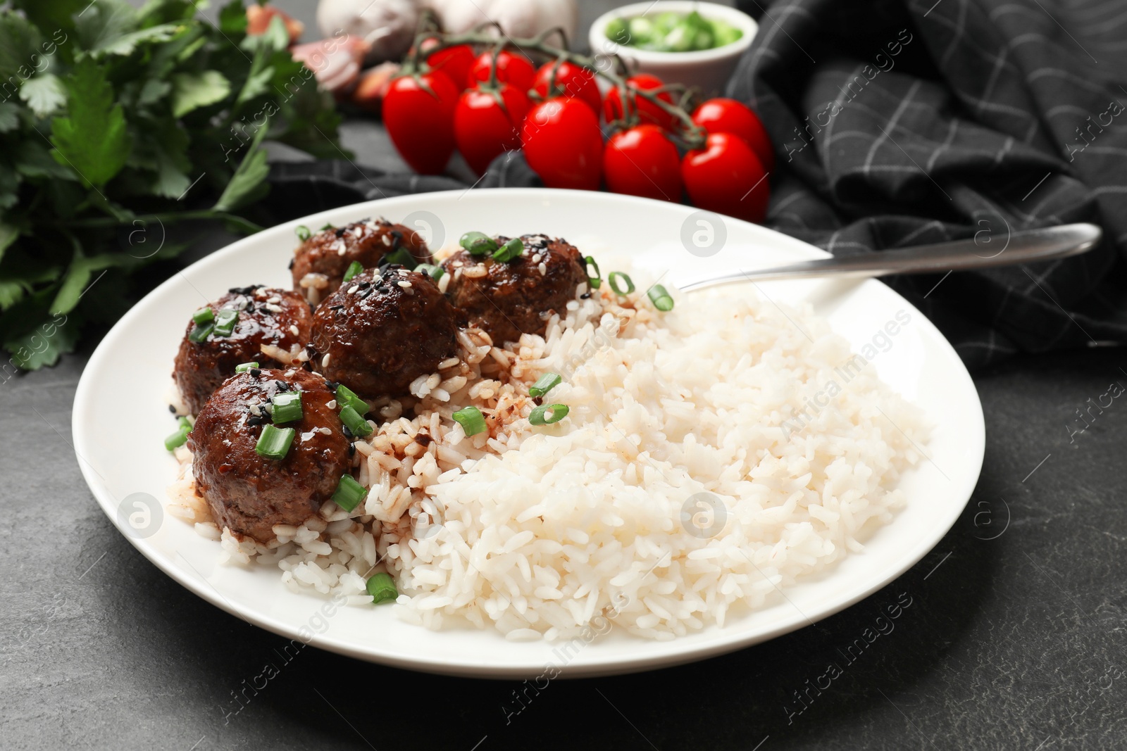 Photo of Delicious rice with meatballs, sauce and green onions on black table, closeup