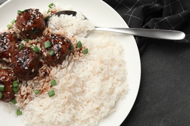 Photo of Delicious rice with meatballs, sauce and green onions on black table, top view