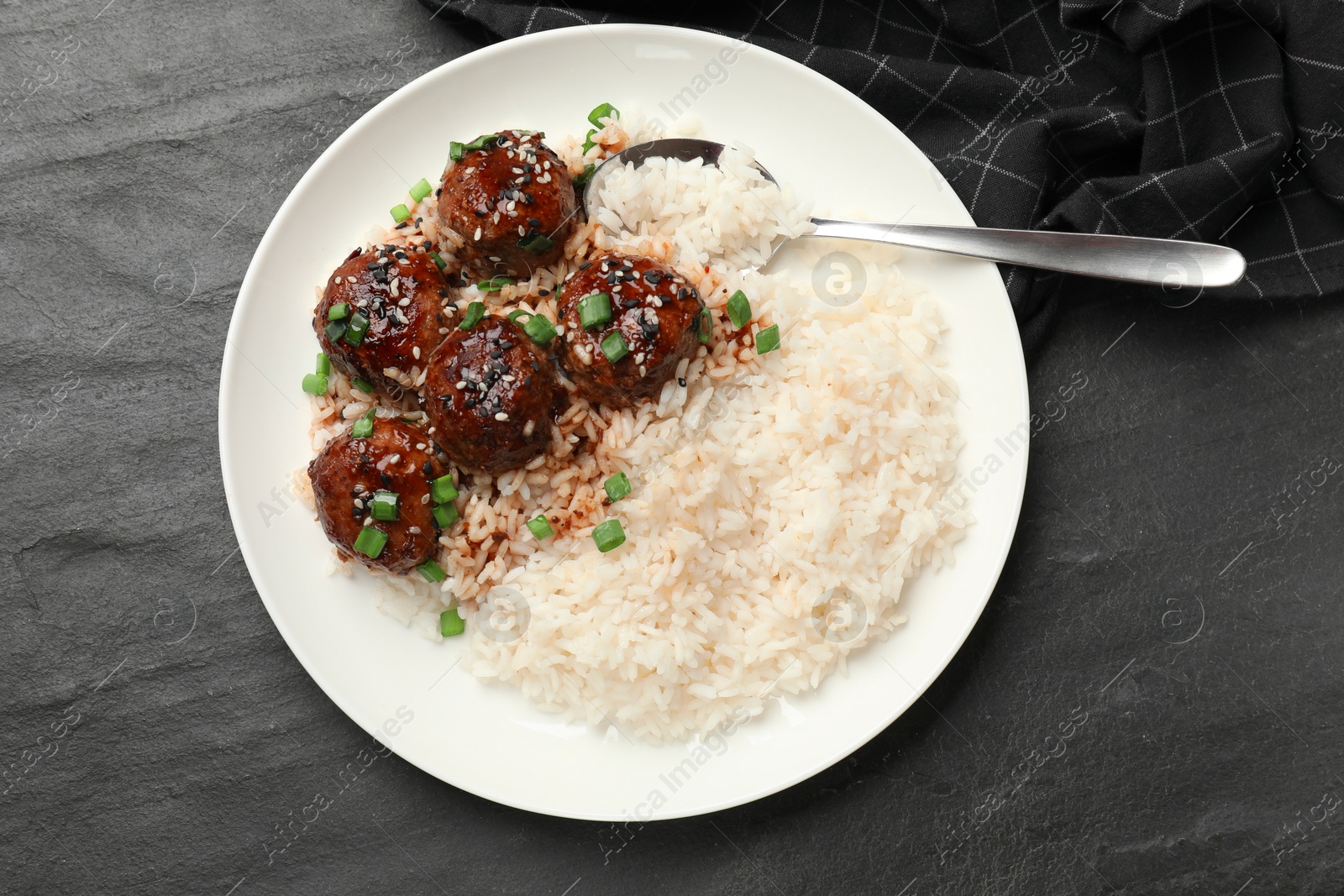 Photo of Delicious rice with meatballs, sauce and green onions on black table, top view