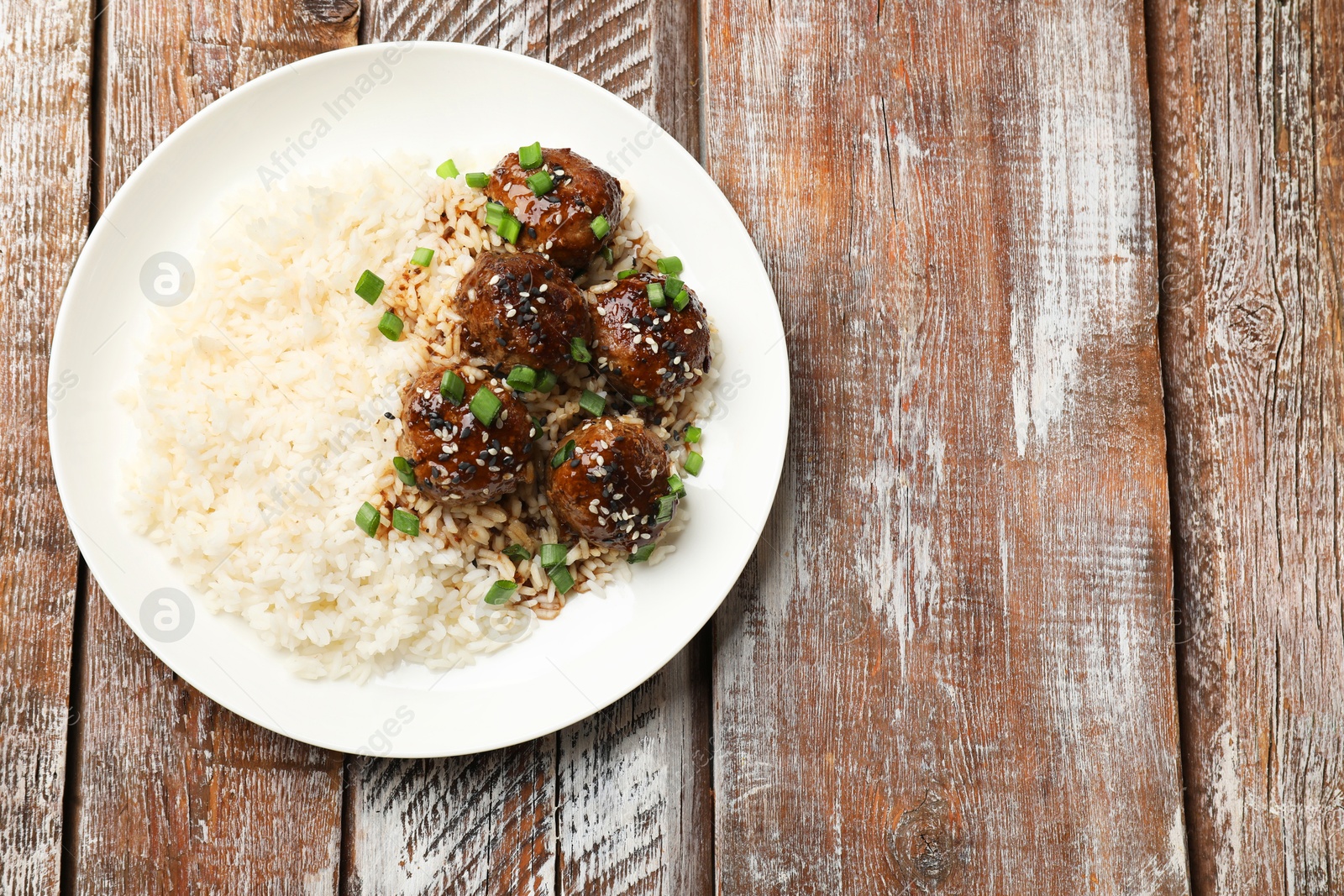 Photo of Delicious rice with meatballs, sauce and green onions on wooden table, top view. Space for text