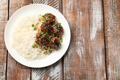 Photo of Delicious rice with meatballs, sauce and green onions on wooden table, top view. Space for text