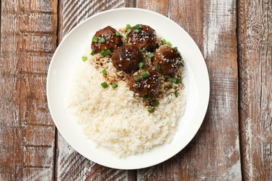 Photo of Delicious rice with meatballs, sauce and green onions on wooden table, top view