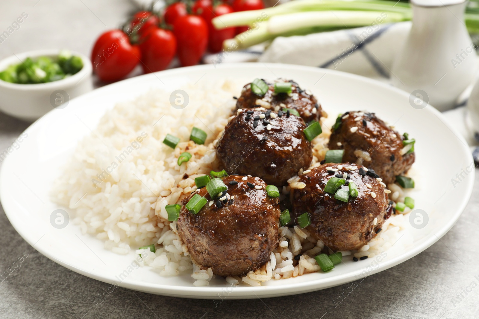 Photo of Delicious rice with meatballs, sauce and green onions on grey table, closeup