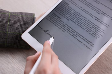 Photo of Electronic signature. Woman using stylus and tablet at wooden table, closeup