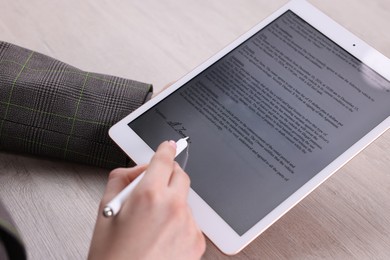 Photo of Electronic signature. Woman using stylus and tablet at wooden table, closeup