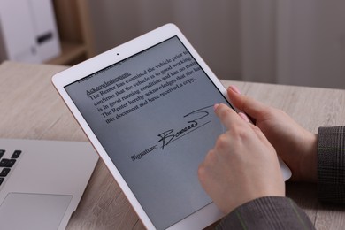 Photo of Electronic signature. Woman using tablet at wooden table, closeup