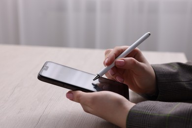 Photo of Electronic signature. Woman using stylus and smartphone at wooden table indoors, closeup