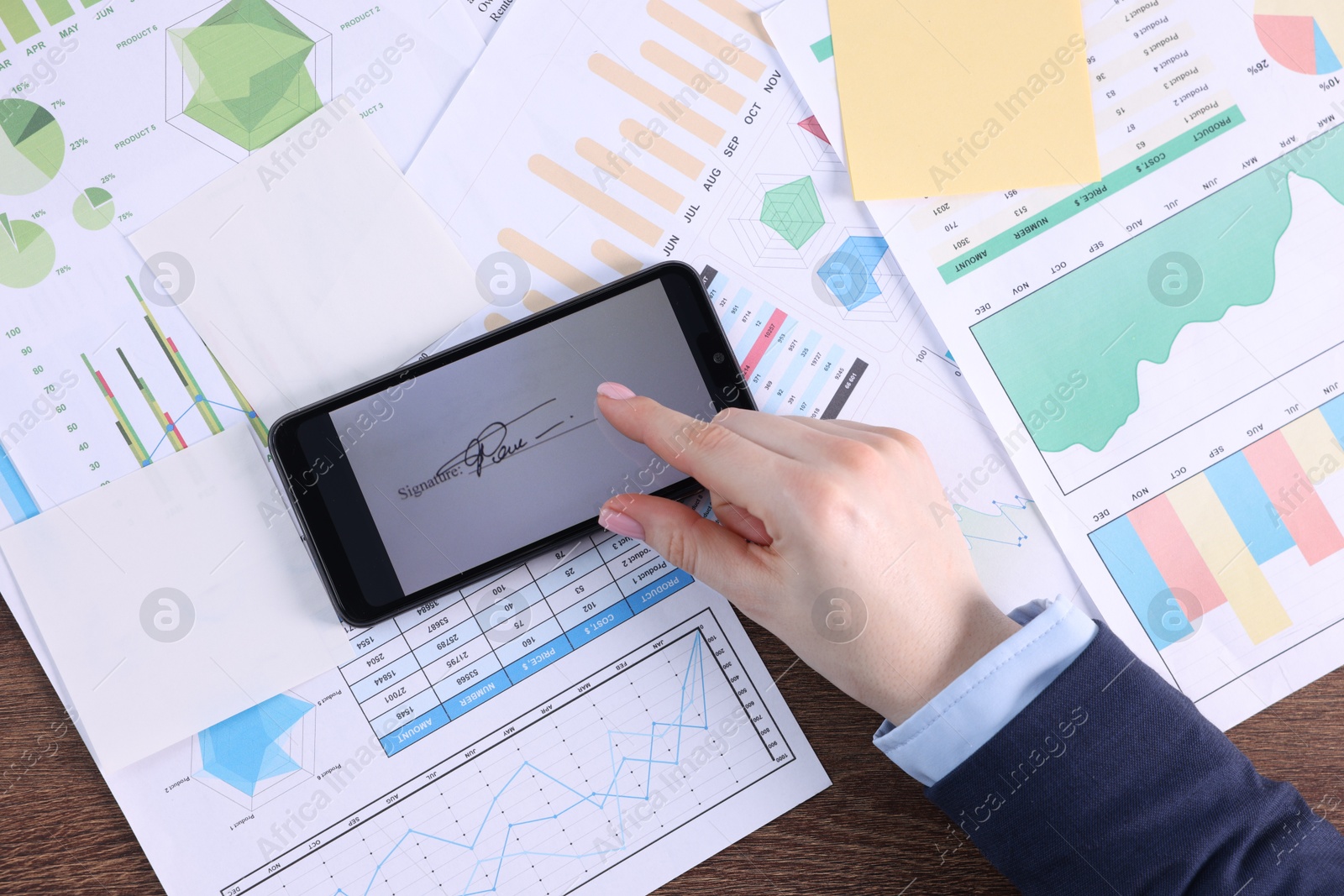 Photo of Electronic signature. Woman using smartphone at wooden table, top view