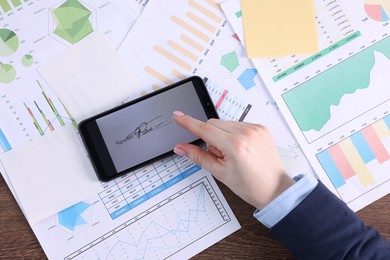 Photo of Electronic signature. Woman using smartphone at wooden table, top view