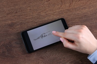 Photo of Electronic signature. Woman using smartphone at wooden table, top view