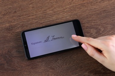 Photo of Electronic signature. Woman using smartphone at wooden table, top view