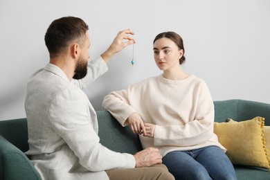 Photo of Psychologist using pendulum while working with patient during hypnosis session indoors