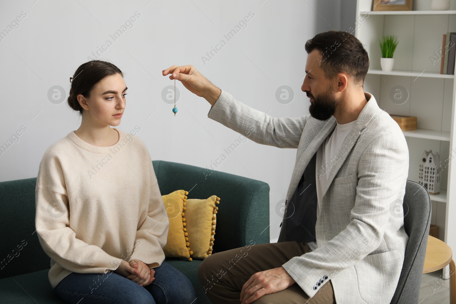 Photo of Psychologist using pendulum while working with patient during hypnosis session indoors