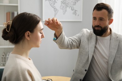 Photo of Psychologist using pendulum while working with patient during hypnosis session indoors