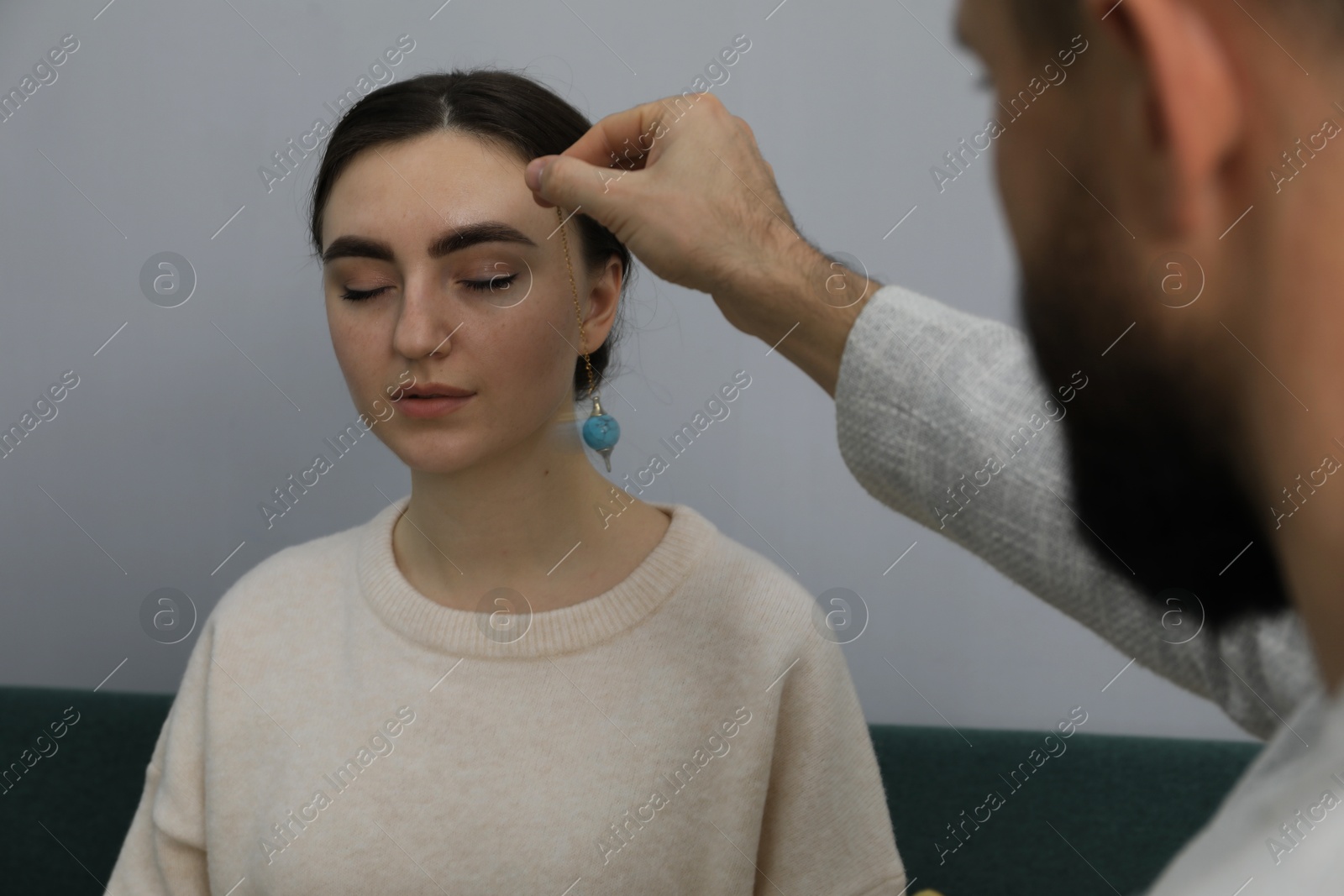 Photo of Psychologist using pendulum while working with patient during hypnosis session indoors, closeup