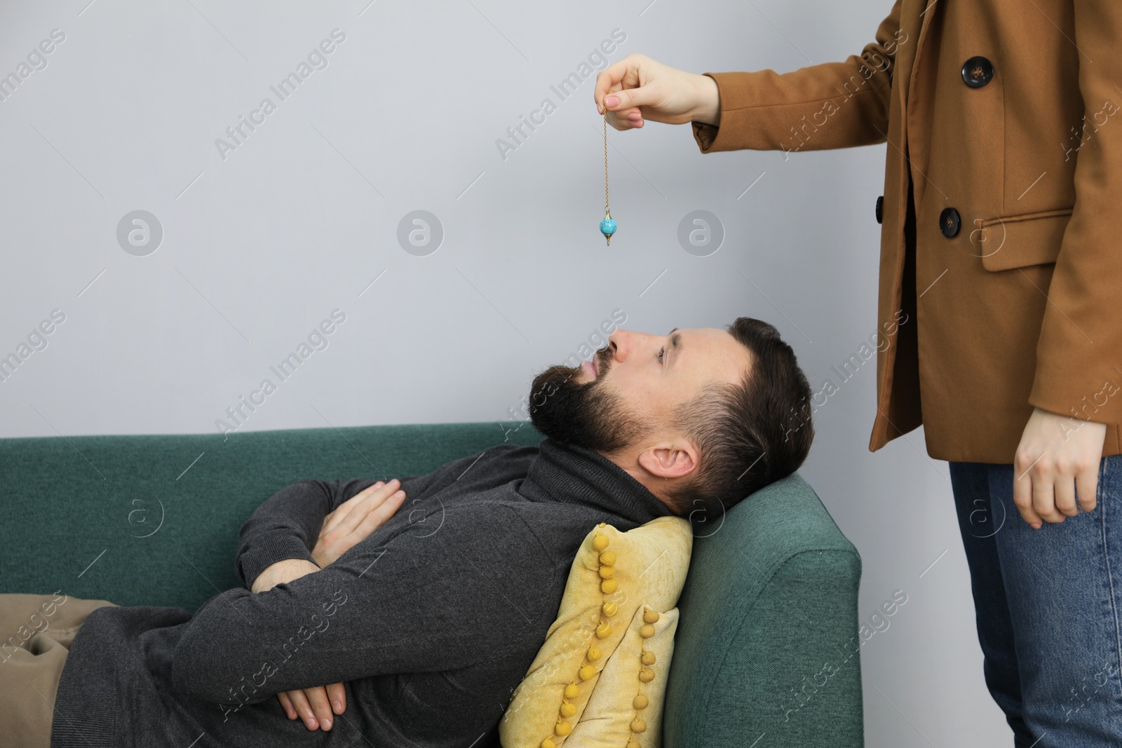 Photo of Psychologist using pendulum while working with patient during hypnosis session indoors, closeup