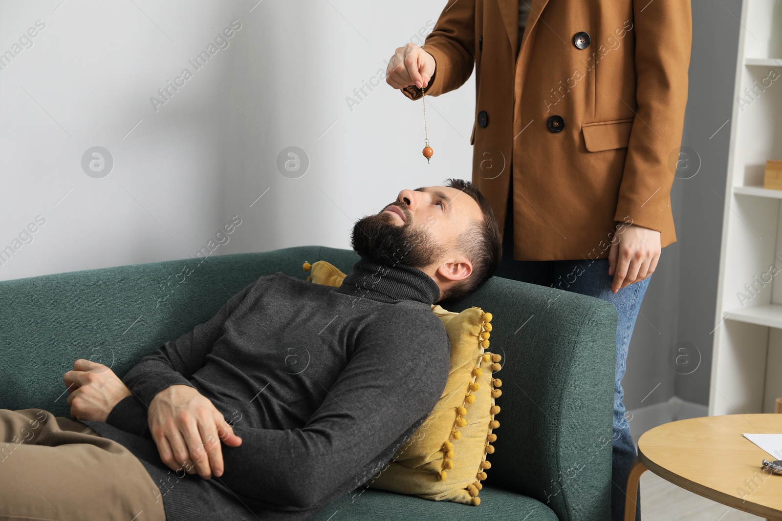 Photo of Psychologist using pendulum while working with patient during hypnosis session indoors, closeup