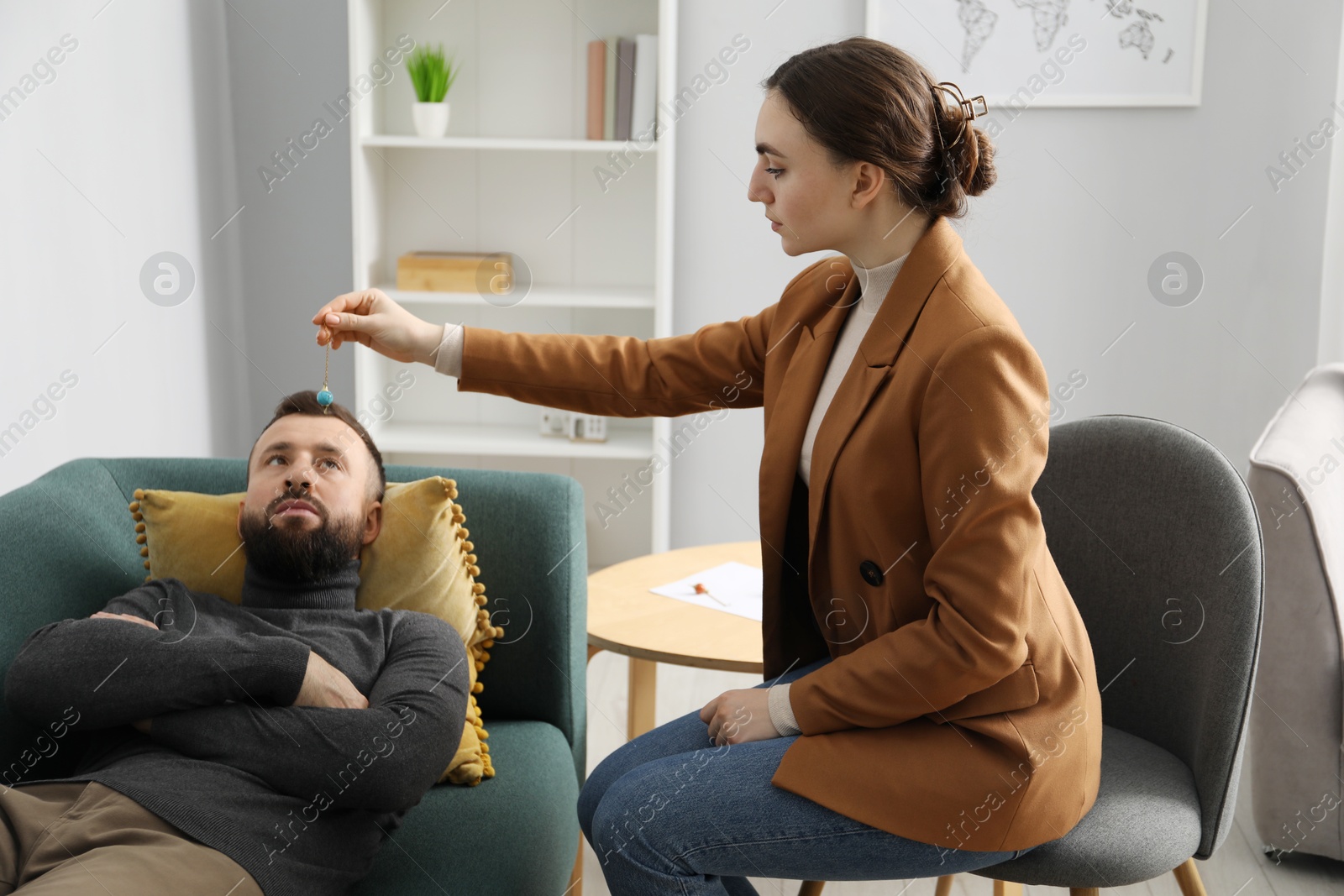 Photo of Psychologist using pendulum while working with patient during hypnosis session indoors