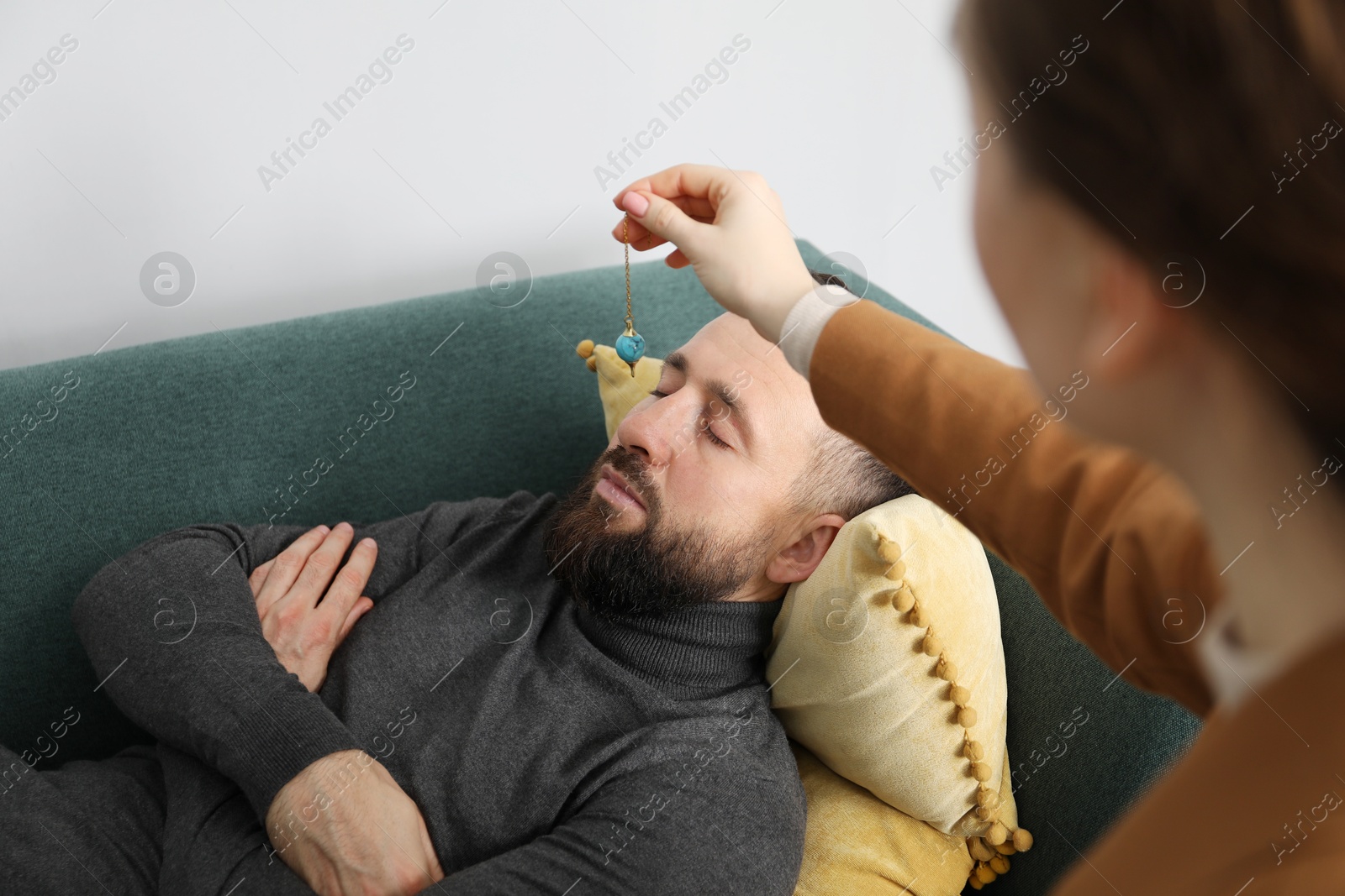 Photo of Psychologist using pendulum while working with patient during hypnosis session indoors, closeup