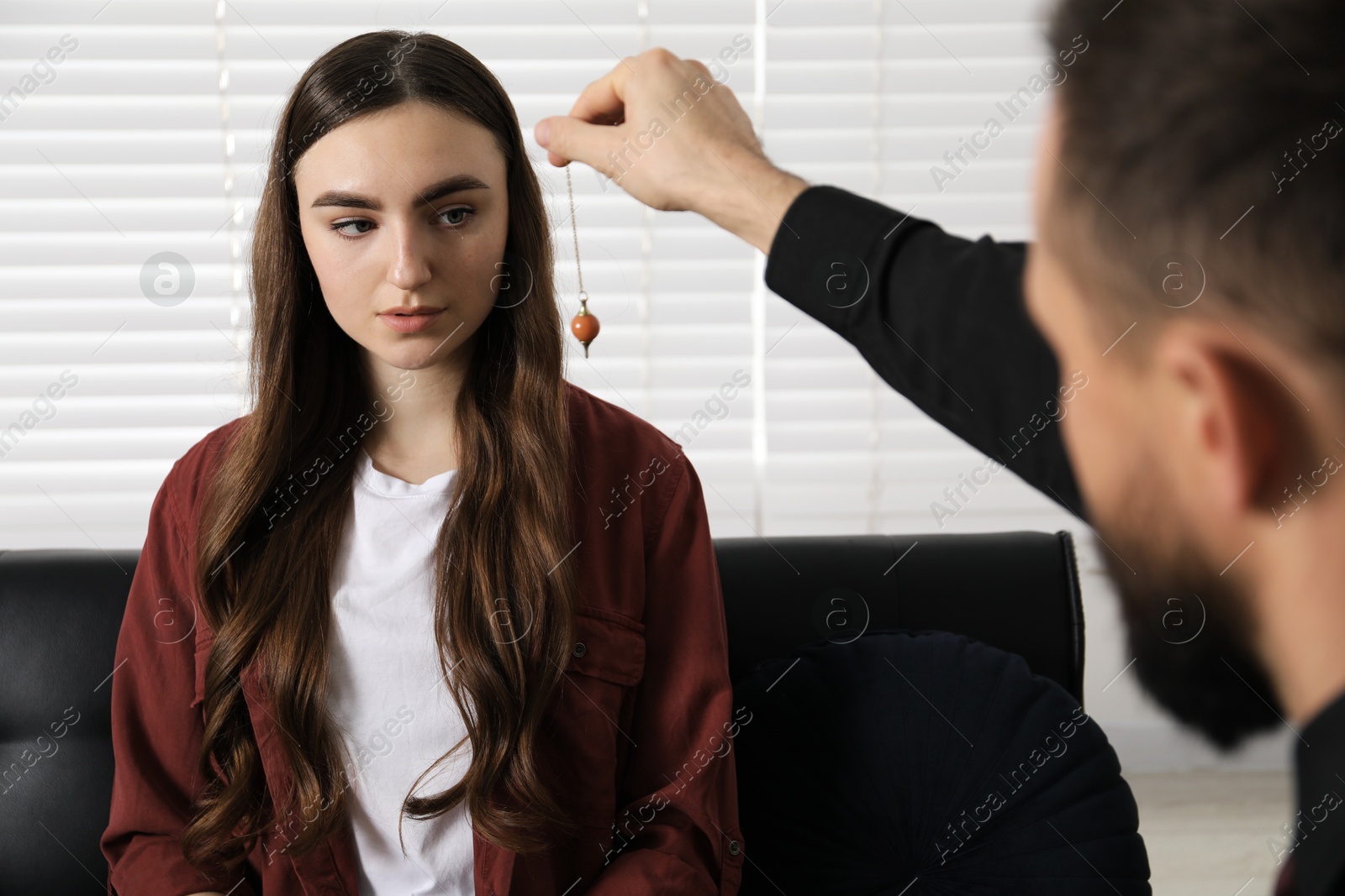 Photo of Psychologist using pendulum while working with patient during hypnosis session indoors, closeup