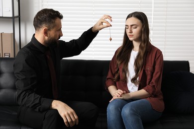 Photo of Psychologist using pendulum while working with patient during hypnosis session indoors