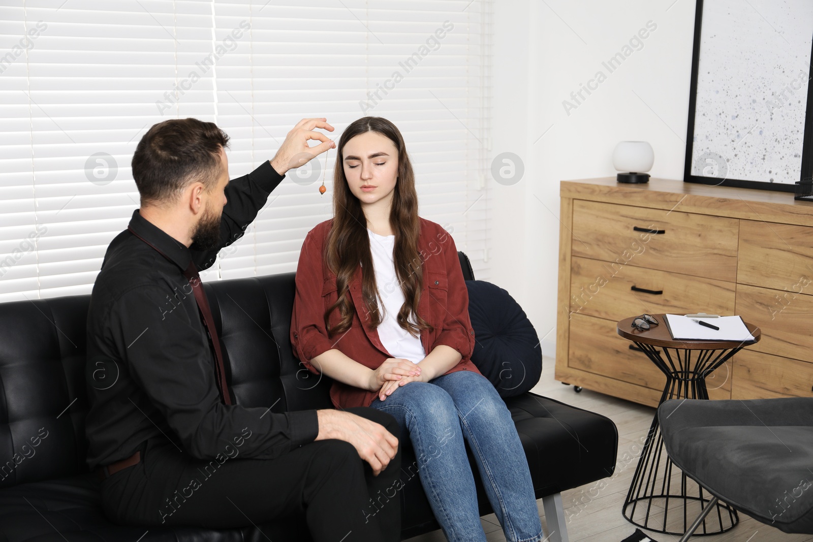 Photo of Psychologist using pendulum while working with patient during hypnosis session indoors