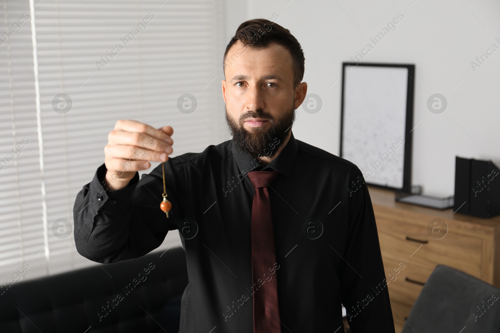 Photo of Hypnosis session. Man with pendulum in office