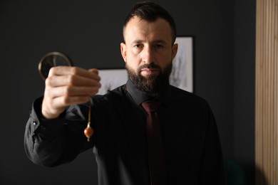 Photo of Hypnosis session. Man with pendulum in office