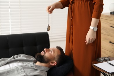 Photo of Psychologist using vintage pocket watch while working with patient during hypnosis session indoors, closeup