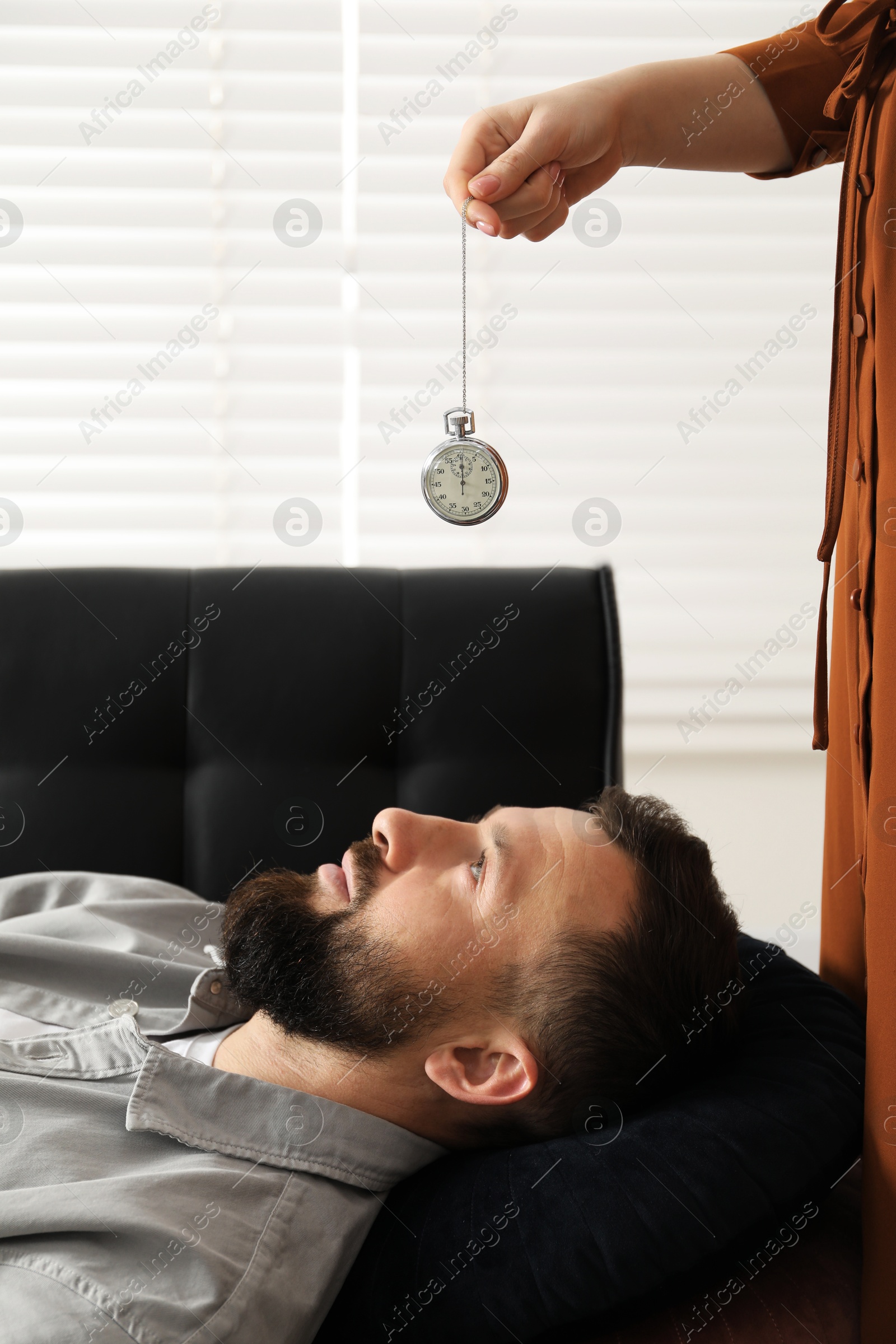 Photo of Psychologist using vintage pocket watch while working with patient during hypnosis session indoors, closeup