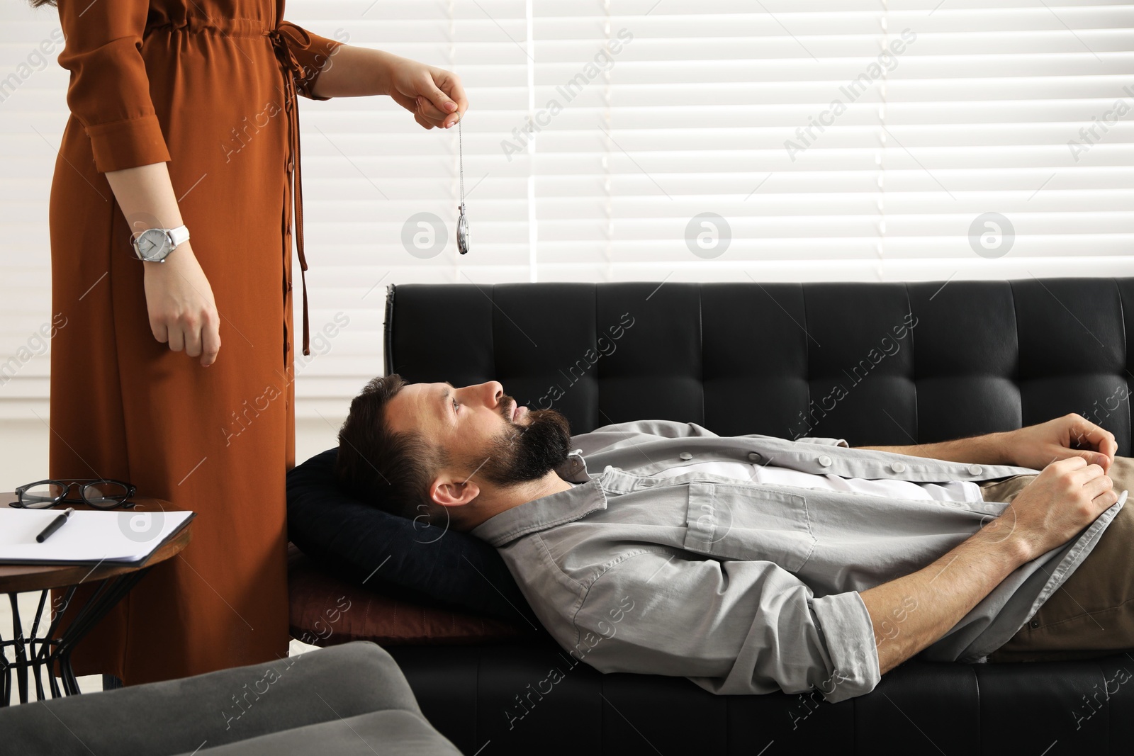 Photo of Psychologist using vintage pocket watch while working with patient during hypnosis session indoors, closeup