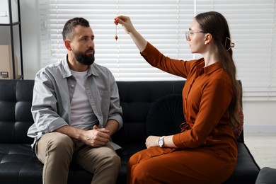 Photo of Psychologist using pendulum while working with patient during hypnosis session indoors