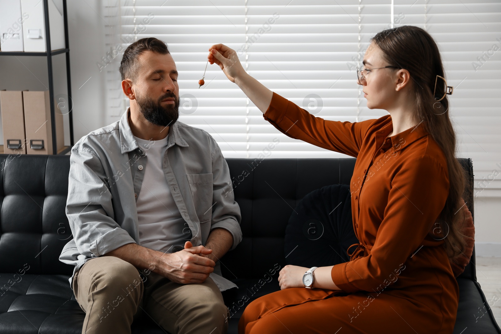 Photo of Psychologist using pendulum while working with patient during hypnosis session indoors