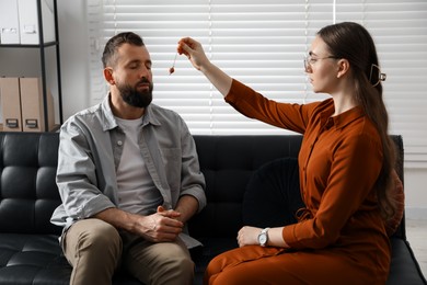 Photo of Psychologist using pendulum while working with patient during hypnosis session indoors