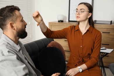 Photo of Psychologist using pendulum while working with patient during hypnosis session indoors