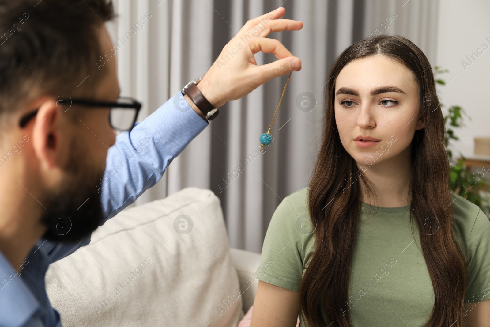 Photo of Psychologist using pendulum while working with patient during hypnosis session indoors, closeup