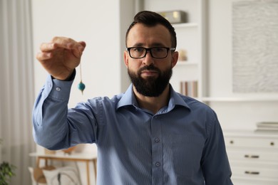 Photo of Hypnosis session. Man in glasses swinging pendulum indoors