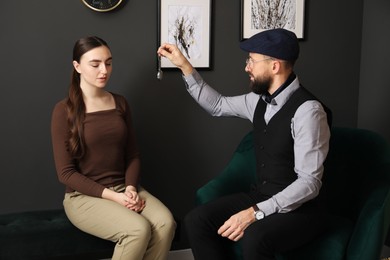 Photo of Psychologist using vintage pocket watch while working with patient during hypnosis session indoors