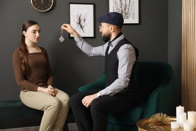 Photo of Psychologist using vintage pocket watch while working with patient during hypnosis session indoors