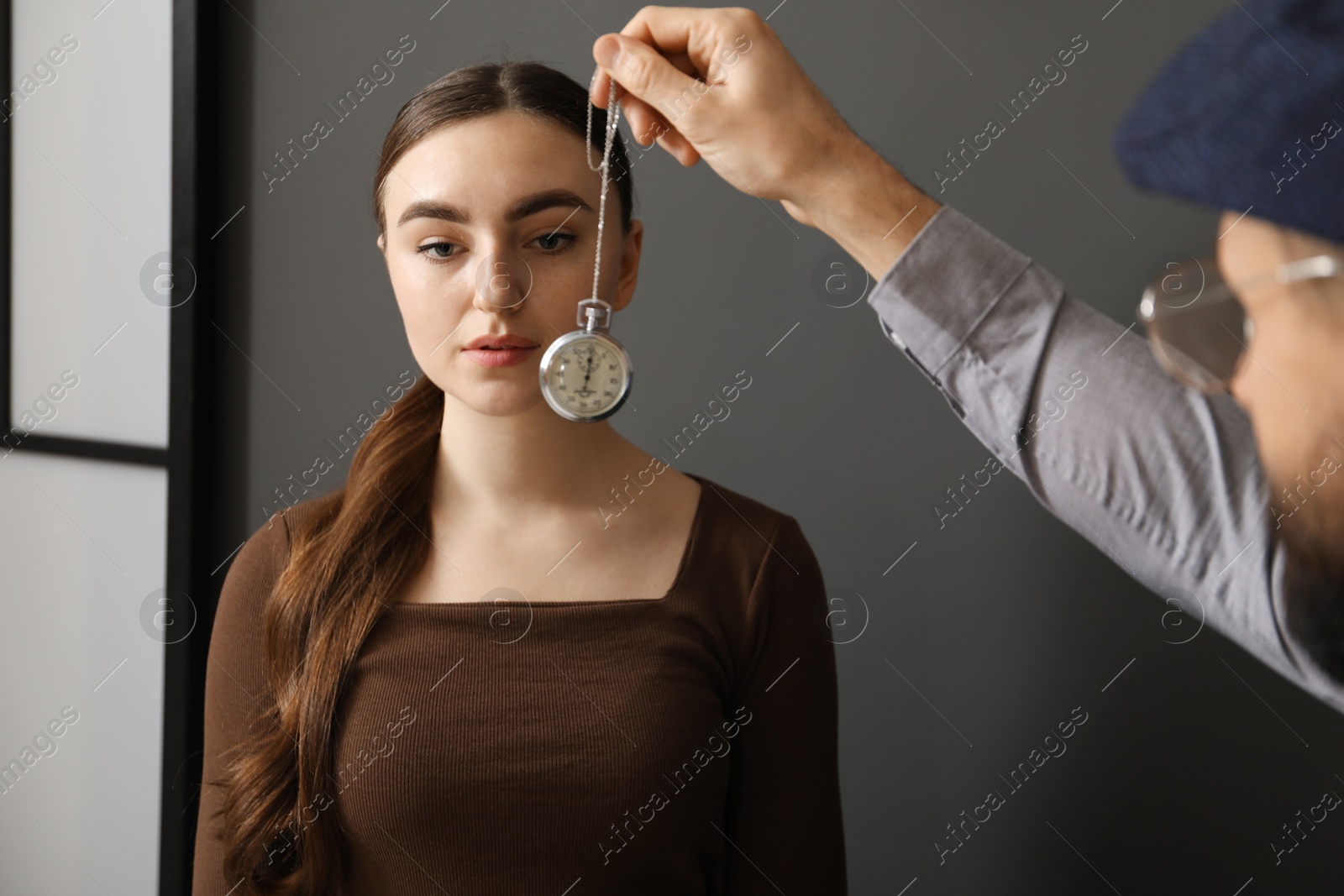 Photo of Psychologist using vintage pocket watch while working with patient during hypnosis session indoors, closeup