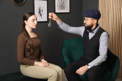 Photo of Psychologist using vintage pocket watch while working with patient during hypnosis session indoors