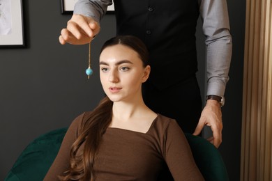 Photo of Psychologist using pendulum while working with patient during hypnosis session indoors, closeup