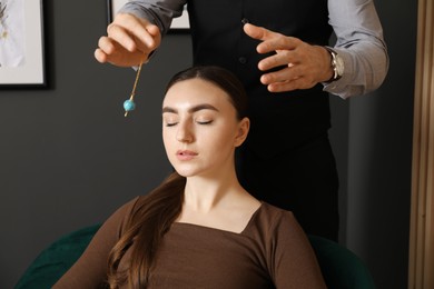 Photo of Psychologist using pendulum while working with patient during hypnosis session indoors, closeup